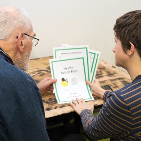 A person with a learning disability being supported by someone to read an easy read document that has been translated by Speak Out