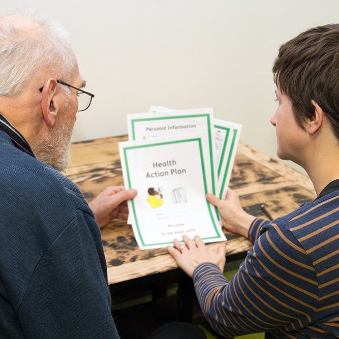 A person with a learning disability being supported by someone to read an easy read document that has been translated by Speak Out